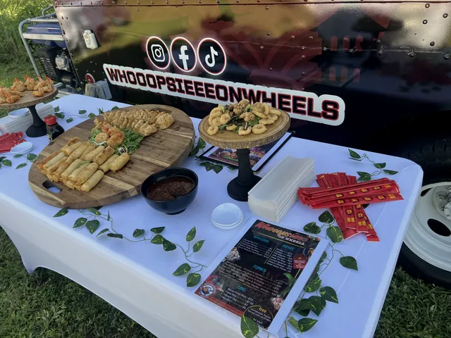 Platters of spring rolls and fried appetizers on a white table in front of the Whooopsieee food truck