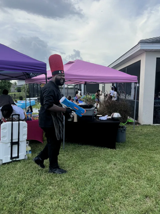 Chef walking across the lawn between party tents with guests gathered behind him