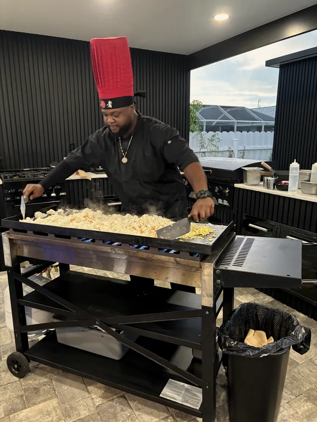 Chef cooking a full flat-top of fried rice on a black grill cart