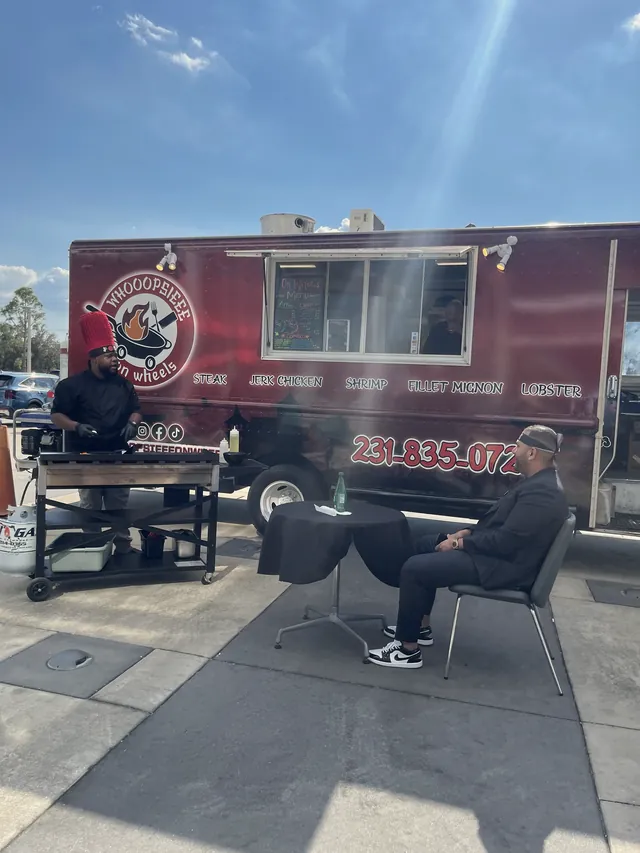 Chef cooking at a grill in front of the red Whooopsieee food truck while a guest waits