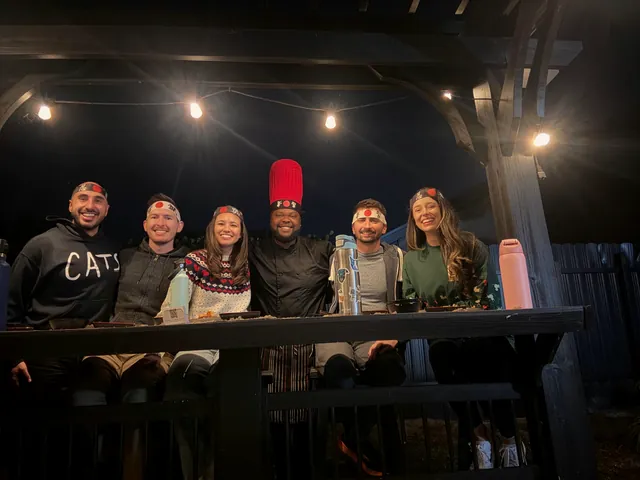 Guests in red and white hibachi headbands posing with the chef at an outdoor bar under string lights