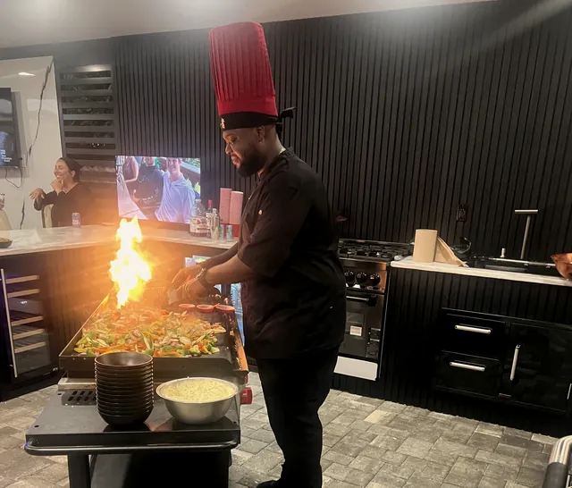 Chef in a red hibachi hat sending a burst of flame off the grill at an indoor kitchen party