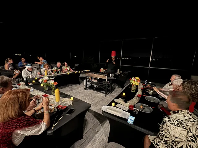 Guests seated at long tables in a screened lanai at night while the chef cooks at the grill