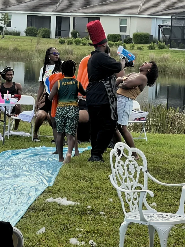 Chef serving a drink hibachi-style to a laughing guest at a lakeside backyard party