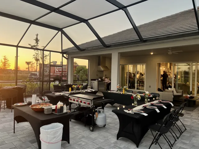 Grill and tables dressed in black, set up in a screened lanai at sunset