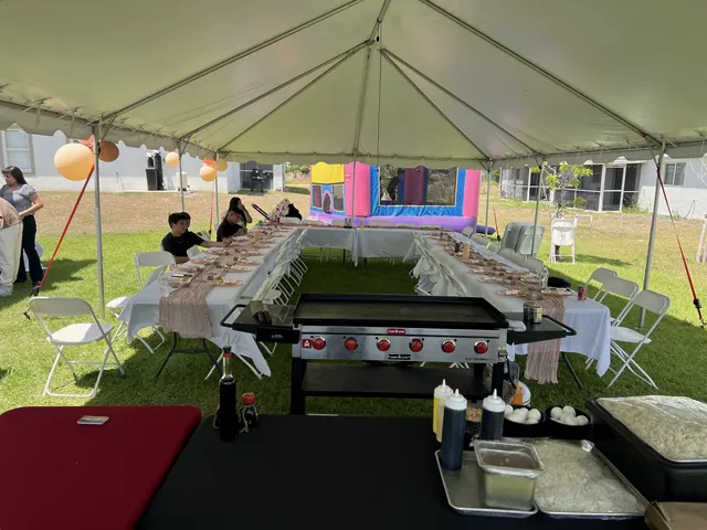 Hibachi grill set up at the head of a long table under a white party tent